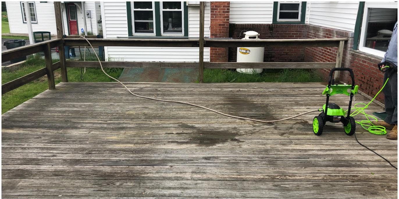 Wide deck with gray, weathered boards and a pressure washer standing ready before cleaning